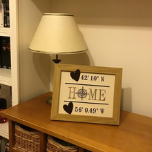 Load image into Gallery viewer, Home Compass GPS embroidered art in a wooden frame on a sideboard with a lamp