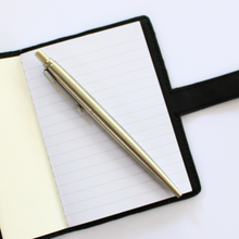 Load image into Gallery viewer, Black notebook cover inside view of lined paper with silver pen