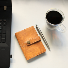Load image into Gallery viewer, Ruler notebook n brown faux leather alongside a pen, laptop and cup