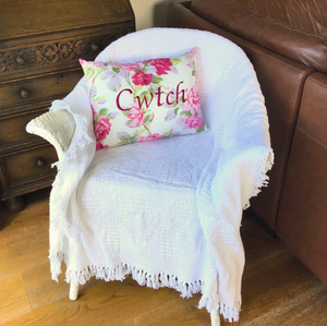 Cwtch cushion in Laura Ashley pink floral fabric on a chair with a white throw
