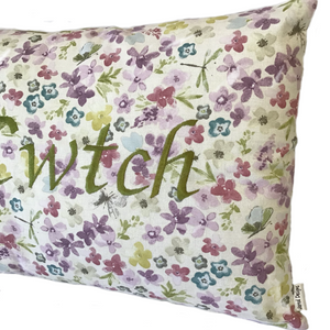 Cwtch cushion stitched in green on floral fabric in close up view
