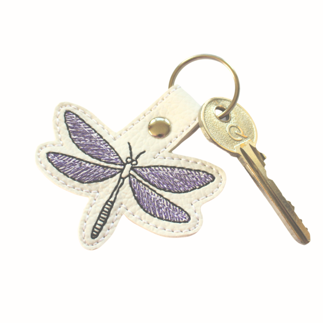 Dragonfly keyfob stitched with purple and black thread on to white faux leather and finished with a chrome metal rivet and split ring with key
