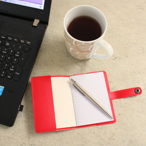 Red notebook open on a desk with a pen, laptop and cup