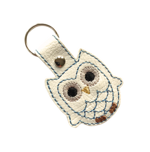 Owl keyfob with blue outline stitching on white faux leather finished with a metal rivet and split ring
