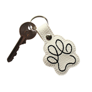 Paw print keyfob in white faux leather with black stitching and key attached