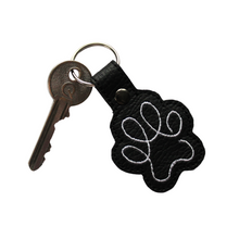 Load image into Gallery viewer, Paw print keyring in black faux leather with white stitching and key attached
