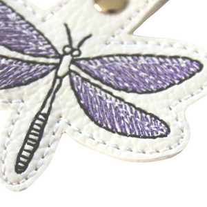 Dragonfly keyfob close up of lower wing stitched in purple and black thread on to white faux leather