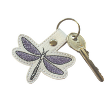 Load image into Gallery viewer, Dragonfly keyfob stitched with purple and black thread on to white faux leather and finished with a chrome metal rivet and split ring with key
