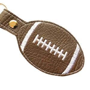 Close up of a rugby ball keyfob with white stitching on brown faux leather with metal rivet